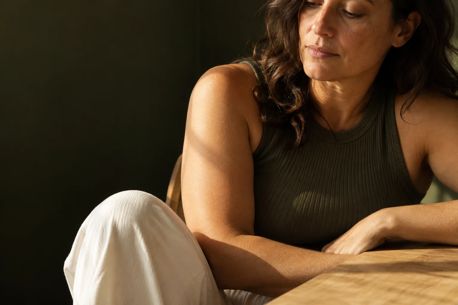 Woman in an olive top sitting by a sunlit table